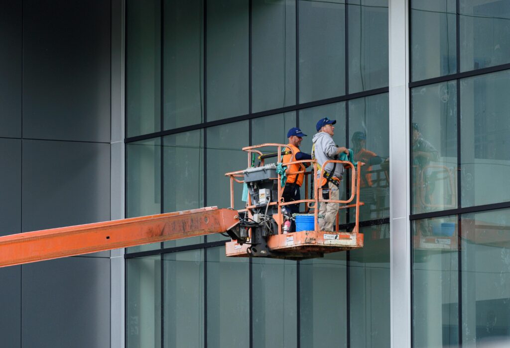 Two workers clean large glass windows using a cherry picker lift outside a building in Canonsburg, PA.
